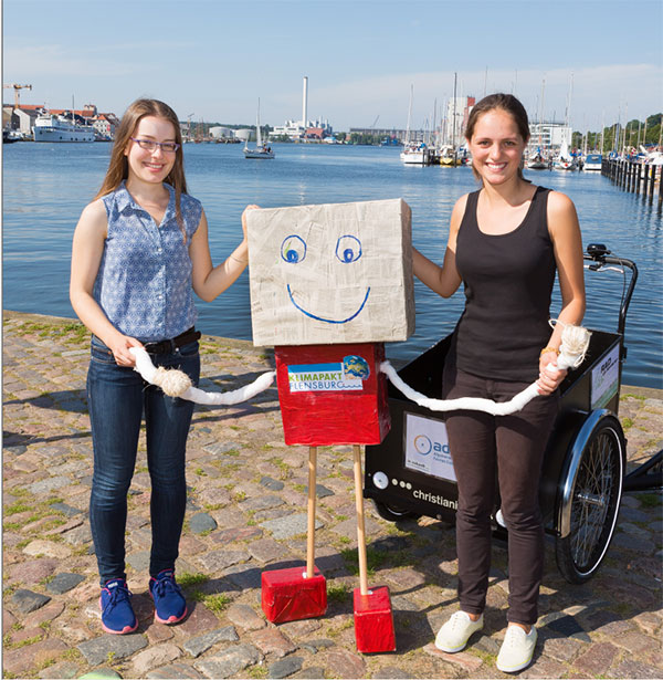 Ann-Kathrin Wild und Helene Wahl (v.l.n.r.) freuen sich zusammen mit dem Klimapakt-Maskottchen auf die zukünftigen Aufgaben für den lokalen Klimaschutz in Flensburg. / Pressebild