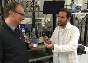 Prof. Elias Klemm (l.) und Doktorand Dennis Kopljar (mit Mikroreaktor in der Hand) vor der Anlage zur elektrochemischen Umsetzung von CO2 / Pressebild: Universität Stuttgart