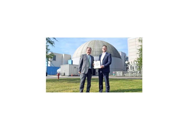 Pressebild: Umweltminister Franz Untersteller (links) übergibt die 4. Abbaugenehmigung an den Chef der EnBW-Kernkraftsparte, Jörg Michels (rechts). Im Hintergrund das Reaktorgebäude des Kernkraftwerks Obrigheim.