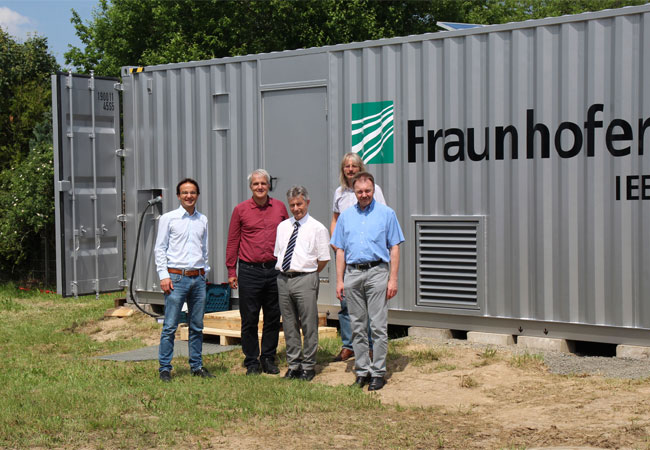 PB: © Fraunhofer IEE Das Kick-Off-Treffen des Projektkonsortiums fand am 5. Juni 2019 im Testzentrum für Intelligente Netze »SysTec« des Fraunhofer IEE statt. Das Foto zeigt Vertreter der Projektpartner vor der neuen Over-Voltage-Ride-Through-Prüfeinrichtung, mit der kurzzeitige Spannungsüberhöhungen auf Mittelspannungsniveau erzeugt werden können. Neben Diskussionen zum Arbeitsplan und zu den konkreten Zielen des Projektes erfolgte auch eine Besichtigung der Laborinfrastruktur zum Themenfeld Netzintegration und Intelligente Netze.