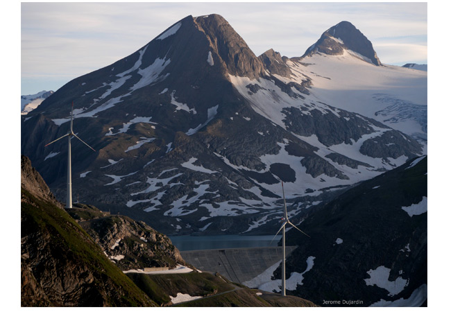 PB: Die Autoren der neuen Studie schlagen vor, die alpine Wasserkraft mit Wind- und Solarenergie zu ergänzen. Windturbinen und Staudamm eines Wasserkraft­werks, Griessee/VS (Foto: Jérôme Dujardin). / Windturbinen und Staudamm, Griessee/VS