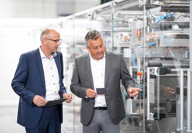 PB: Werner Volk, Leiter neue Anwendungen/Konzepte bei Optima Life Science (links) und Jürgen Bareiß, Leiter des Geschäftsbereichs Optima Life Science, vor einer im Bau befindlichen Produktionsanlage für Membran-Elektroden-Anordnungen (MEAs). / Quelle: Optima