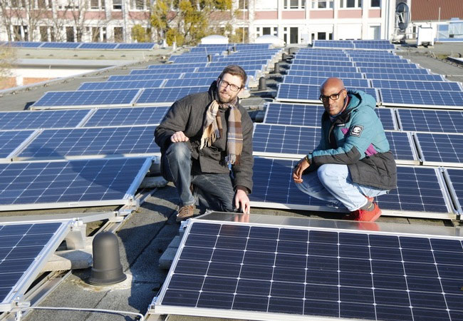 PB: Christian Hachmann (links) und Manuel Valois mit einer Photovoltaikanlage auf dem Dach des Standorts Wilhelmshöher Allee der Uni Kassel. Aufgabe des Kasseler Projektteams ist es unter anderem, die effiziente und stabile Netzintegration solcher Erzeuger erneuerbarer Energien zu modellieren / Foto: © Uni Kassel.