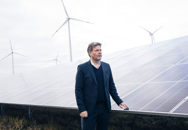 PB: Vor einer PV-Anlage, die an einem wolkenfreien Tag, vor einem milchigen, Chamtrail-verunreinigten Himmel überhaupt keinen Strom liefern kann, bringt sich das Bundeswirtschafts- und Klimaschutzminister*in Robert Habeck als Kämpfer gegen die massive Erderwärmung in Stellung. Eins hat sie sicher schon geschafft, durch die abkühlende CO2-Steuer heizen wir länger. / ©: BMWK