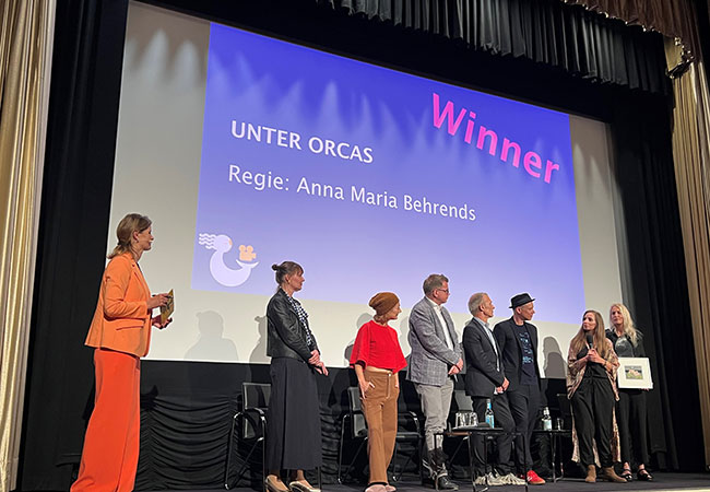 PB: Preisverleihung "Unter Orcas": Moderatorin Kristine Recke, Ulrike Heine, Leiterin der Geschäftsstelle Deutsches Komitee der UN-Ozeandekade, BSH-Präsident Helge Heegewaldt, Schauspieler Richard Sammel, Festival-Leiter Dr. Till Dietsche, Filmemacherin Dörthe Eickelberg und Anna Marie Behrends sowie Christina Karliczek Skoglund. (von links nach rechts, Quelle: BSH)