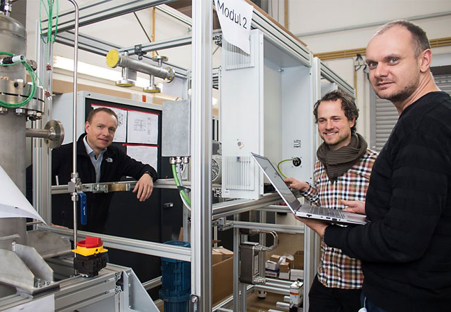 PB: Die WTZ-Experten Carsten Tietze, Samuel Brinnig und Martin Steiner (v.l.) am LOHC Wasserstoffspeicher, der gerade aufgebaut wird. / © Foto: K.Graubaum