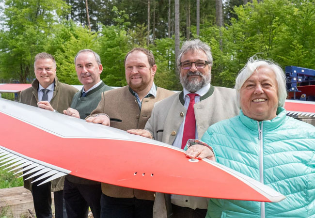 PB: Bayerns Energieminister Hubert Aiwanger gemeinsam mit Martin Neumeyer (Vorstandsvorsitzender BaySF, 1.v.l.), Peter Wagner (1. Bürgermeister Gemeinde Aying, 3.v.l.), Michael Falkenhahn (1. Bürgermeister Gemeinde Otterfing, 4.v.l.) und Barbara Bogner (1. Bürgermeisterin Sauerlach, 5.v.l.) am Rotorblatt für das dritte Windrad im Hofoldinger Forst. Foto: StMWi/B. Brummer